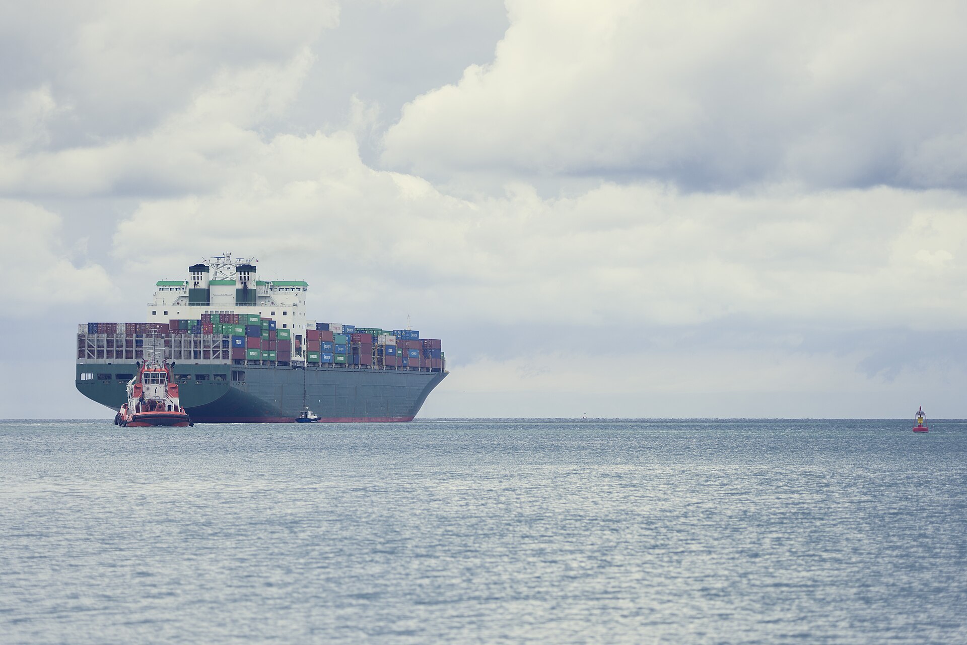 Navio porta-contêiner carregado sendo escoltado por rebocador